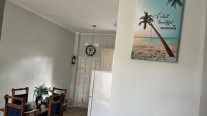 Un coin repas avec une table et des chaises en bois, un vase rempli de fleurs et un tableau représentant une scène de plage, accroché au mur.