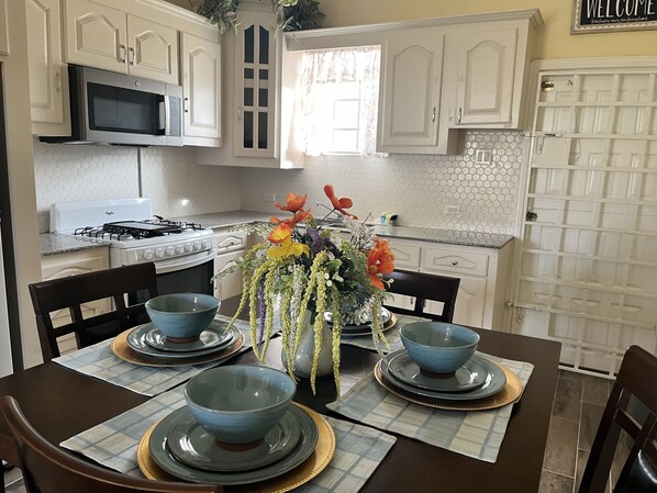 Una cocina con armarios blancos, estufa, microondas y una mesa de comedor con fuentes y platos azules.