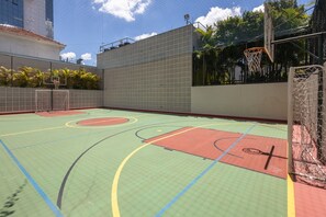 Enjoy a game of basketball under the open sky on our outdoor court, surrounded by lush greenery and a nearby building.