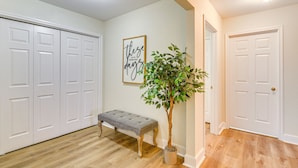 A hallway with a bench, a potted plant, and a framed quote on the wall.