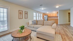 A spacious living room with a beige sectional sofa, a round wooden coffee table, and a potted plant.