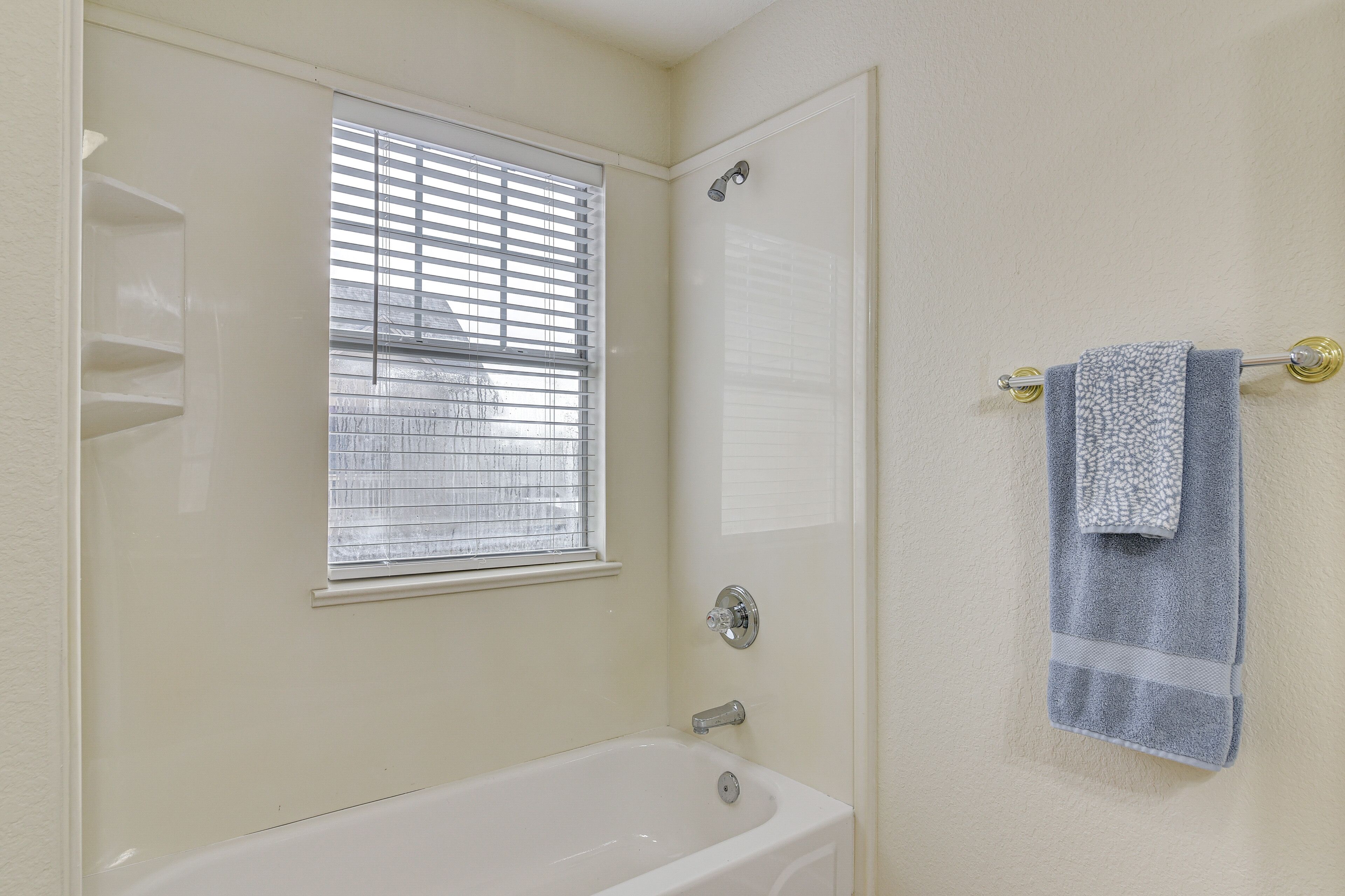 A bathroom with a bathtub, a window with blinds, and a towel rack with a towel.