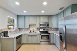 Una cocina moderna con armarios grises claros, electrodomésticos de acero inoxidable y un ventanal que proporciona luz natural.