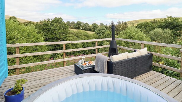 Eine Holzterrasse mit Whirlpool, Gartenmöbeln und Blick auf eine üppige Landschaft.