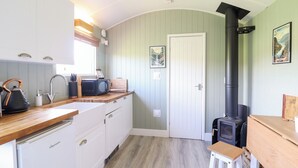 Eine kompakte Küche mit weißen Schränken, einer Holz Arbeitsplatte, einem eingebauten Herd und einem kleinen Hocker.