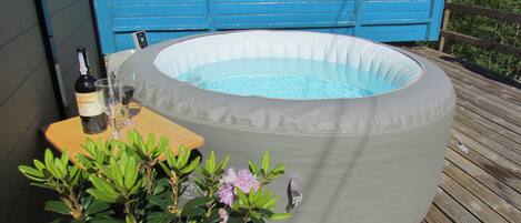 Un jacuzzi gonflable installé sur une terrasse en bois, avec une bouteille de vin et des verres.
