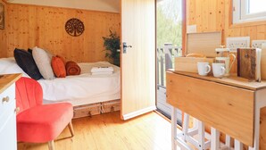 Um quarto de cabana aconchegante, com uma cama, uma cadeira vermelha, uma escrivaninha de madeira e uma janela com vista para o verde.