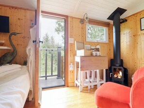 Hyggelig interiør i en hytte med træpaneler, en seng, et skrivebord, en stol og en brændeovn.