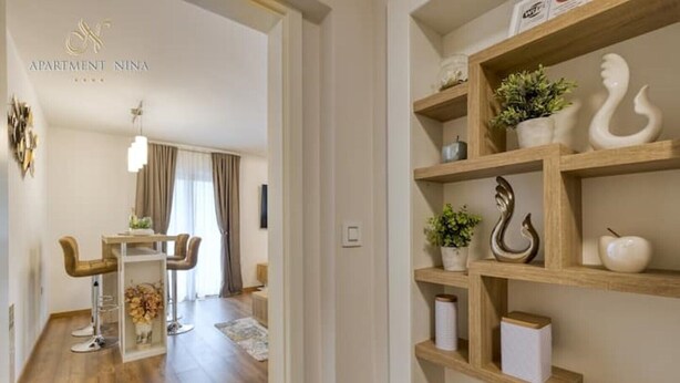 A modern apartment interior with a dining area, a wooden shelf with decorative items, and a visible logo for 'Apartment Nina'. - Apartment Nina Pazin - In the heart of Istria. Close to all tourist attractions (Pazin)