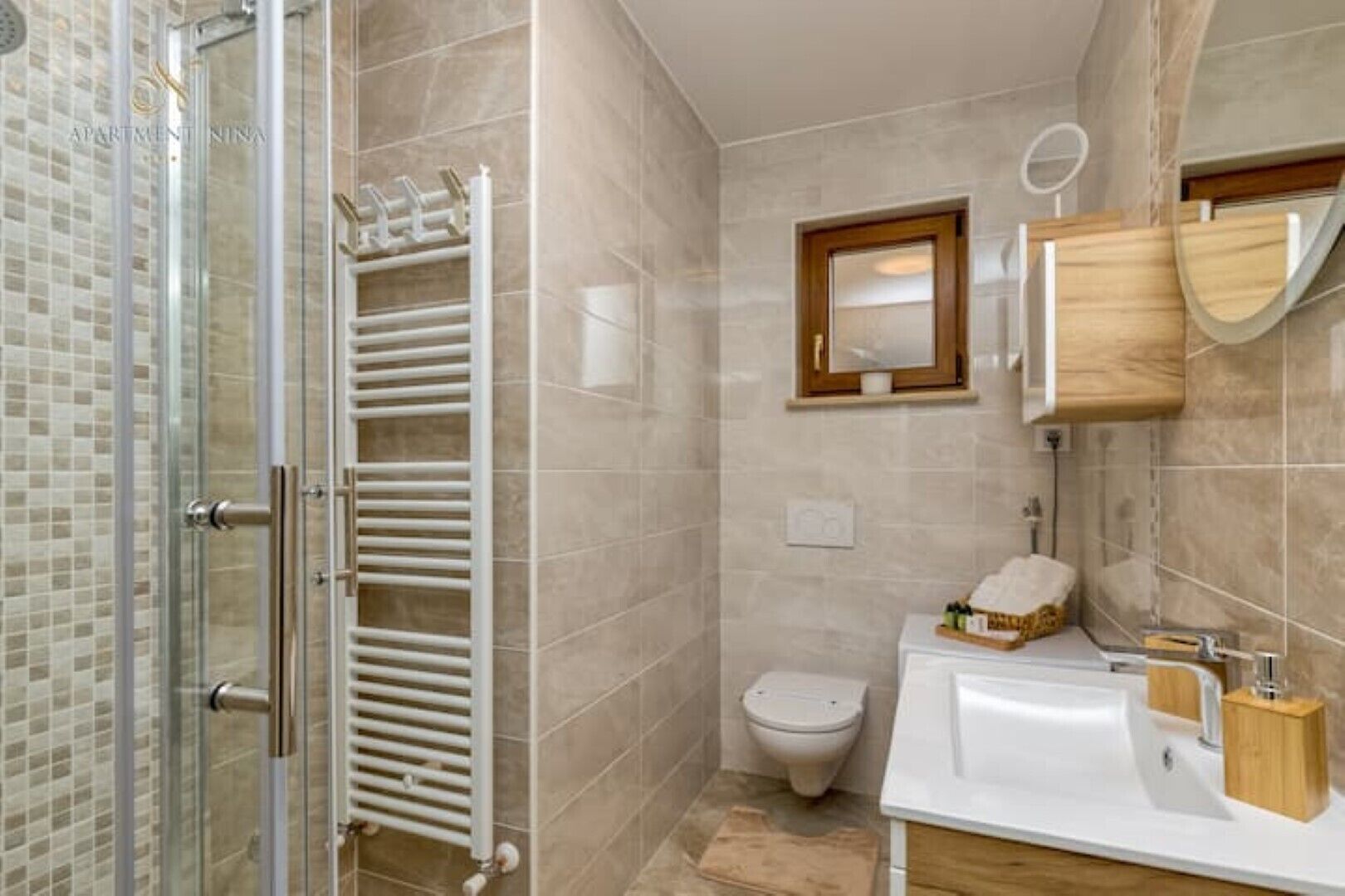 A bathroom with a glass shower enclosure, a white sink with wooden accents, a toilet, and a towel rack.