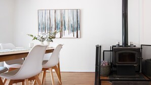A modern dining area with a wooden table and white chairs, a painting above the table, and a black wood-burning stove. - Nirvana - Escape from urban chaos to relish all the region has in store. (Porepunkah)