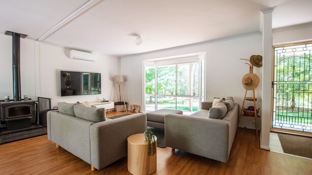 A modern living room with a fireplace, grey sofas, a TV, and a large window with a view of greenery. - Nirvana - Escape from urban chaos to relish all the region has in store. (Porepunkah)