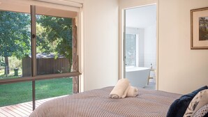 A bedroom with a large window, a view of a garden, and a bathroom visible through an open door. - Nirvana - Escape from urban chaos to relish all the region has in store. (Porepunkah)