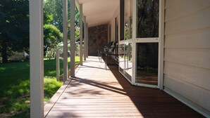 A covered wooden deck with a stone wall and glass doors leading to a garden. - Nirvana - Escape from urban chaos to relish all the region has in store. (Porepunkah)