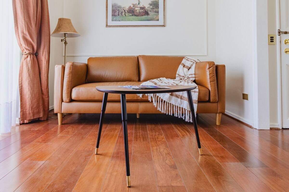 Ein Wohnzimmer mit braunem Ledersofa, einem kleinen runden Tisch mit Lampe und einem gerahmten Bild an der Wand.