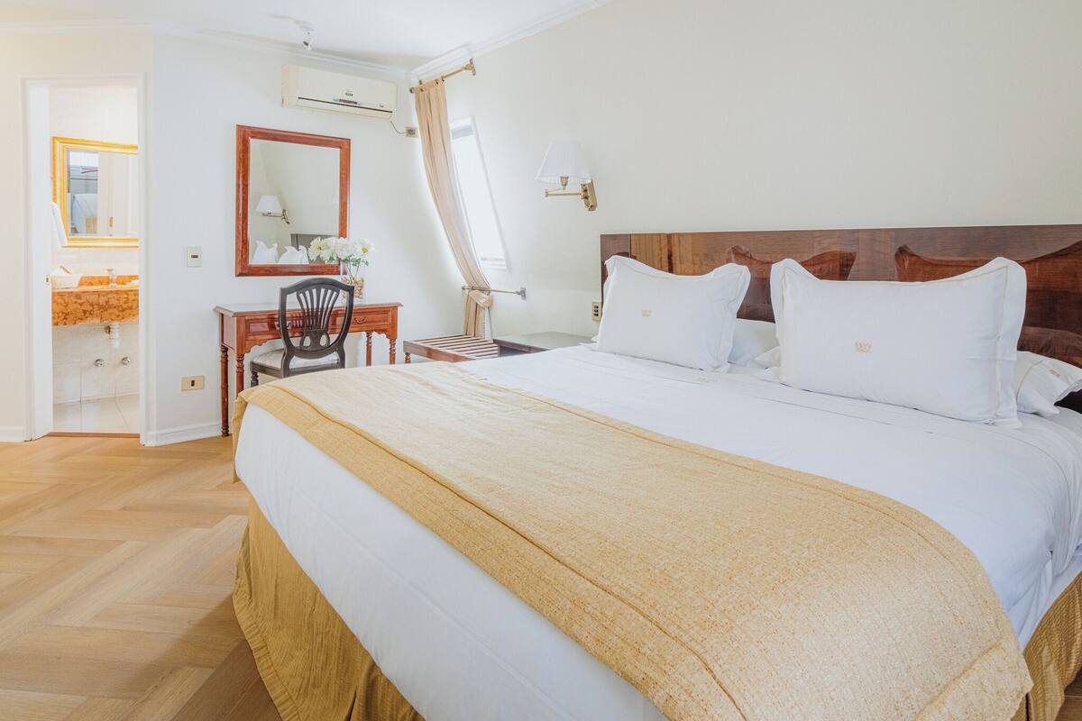 Ein Hotelzimmer mit einem großen Bett, einem Schreibtisch mit Stuhl, einem Spiegel und einem Fenster mit Vorhängen.