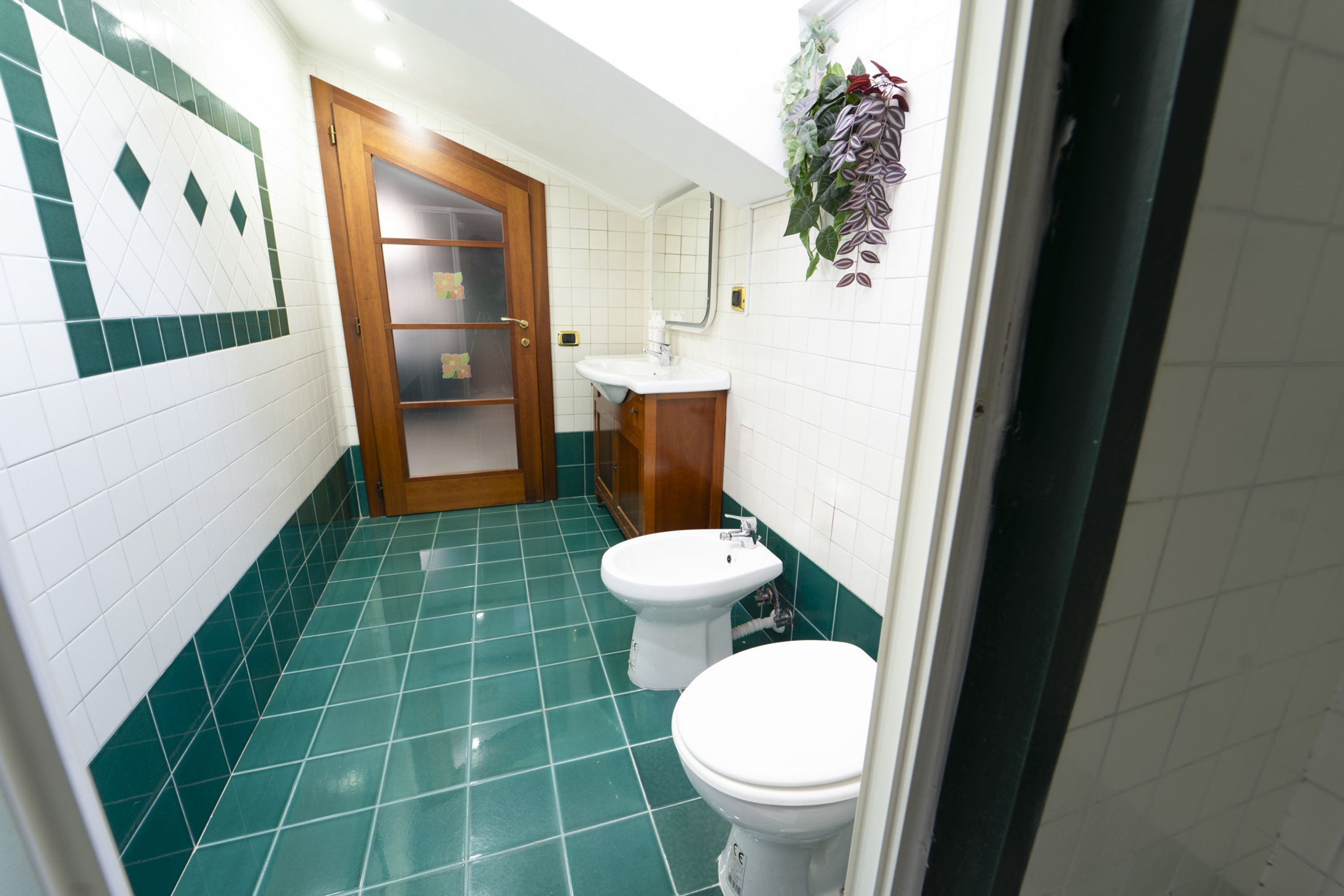 A bathroom with green tiles, a white toilet, a sink, and a wooden door.