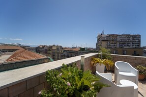 Une terrasse sur le toit agrémentée de plantes en pot, de meubles d’extérieur blancs et offrant une vue sur les bâtiments environnants.