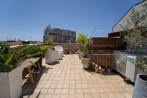 Une terrasse sur le toit, aménagée avec du mobilier d’extérieur, des plantes en pot et un climatiseur de la marque Hisense.