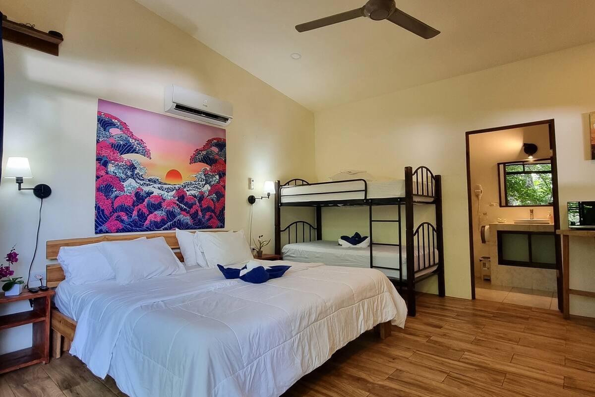 A bedroom with a bunk bed, a ceiling fan, an air conditioning unit, and a painting of waves.