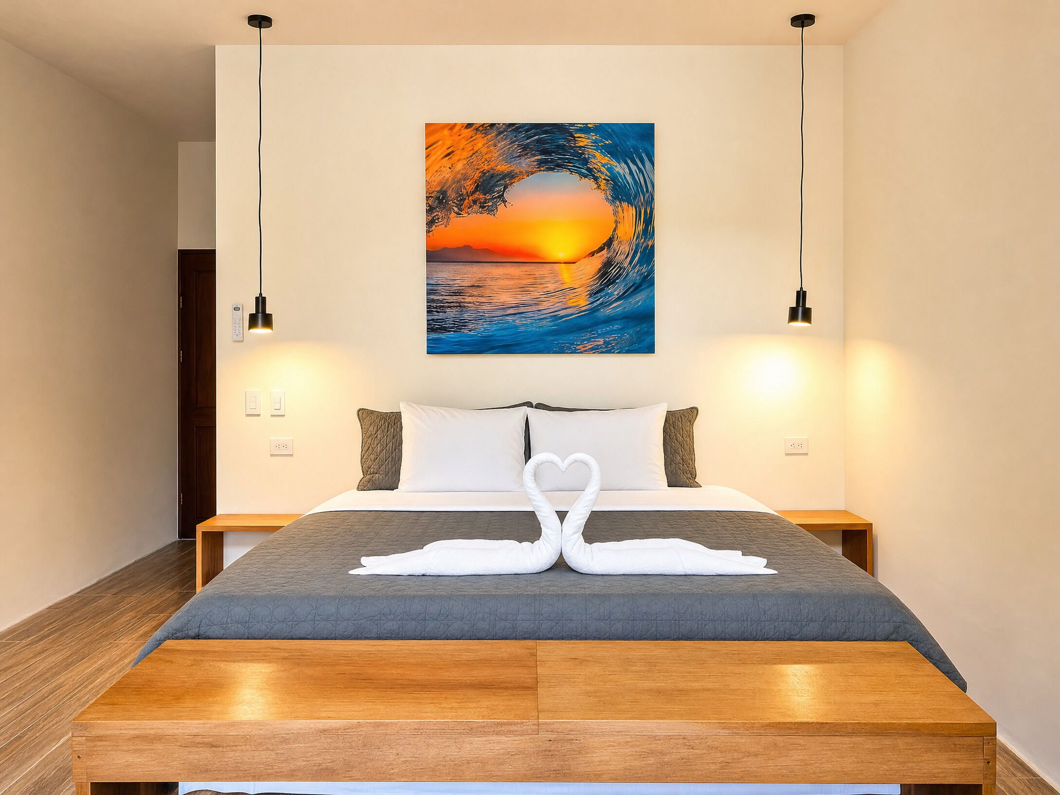 Habitación de hotel con cama, un cuadro de un atardecer sobre el agua y dos lámparas de noche.