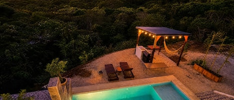 A swimming pool with a deck, lounge chairs, and a covered seating area with string lights.