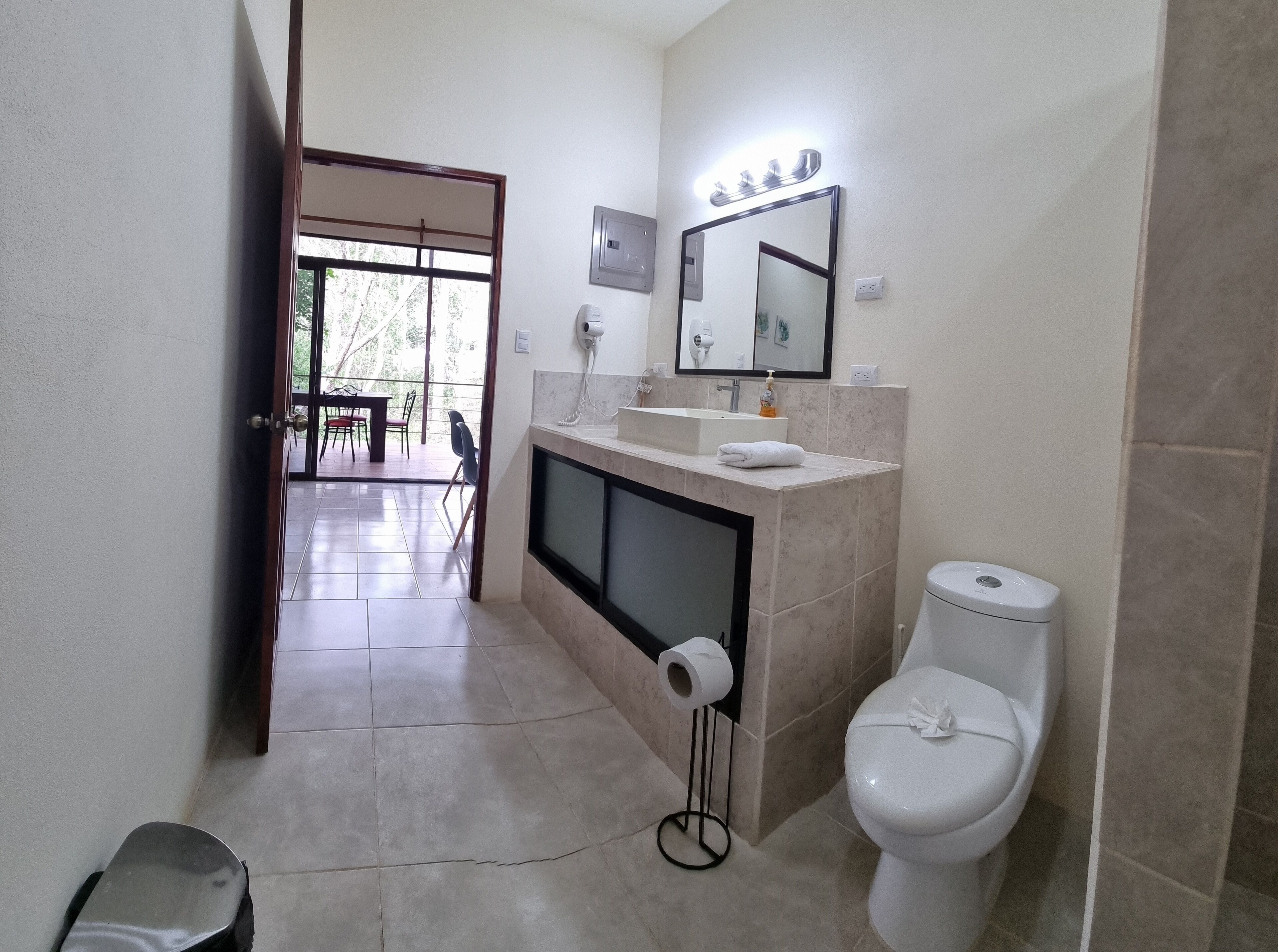 Un bagno con il water, un lavandino e uno specchio. C'è un asciugamano sul lavandino e un porta carta igienica.