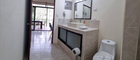 Un bagno con il water, un lavandino e uno specchio. C'è un asciugamano sul lavandino e un porta carta igienica.