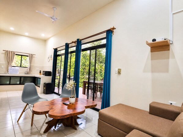 A modern living room with a wooden dining table, two chairs, a sofa, and a ceiling fan.