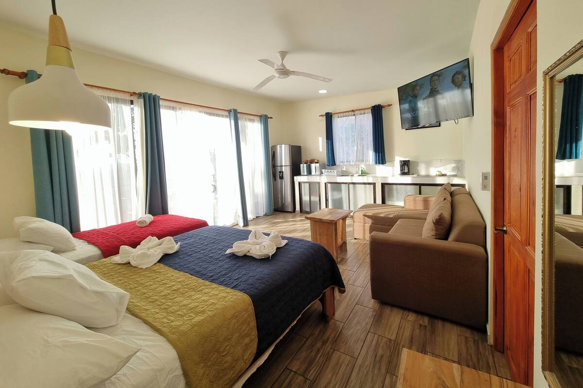A hotel room with two beds, a sofa, a kitchenette, and a TV.