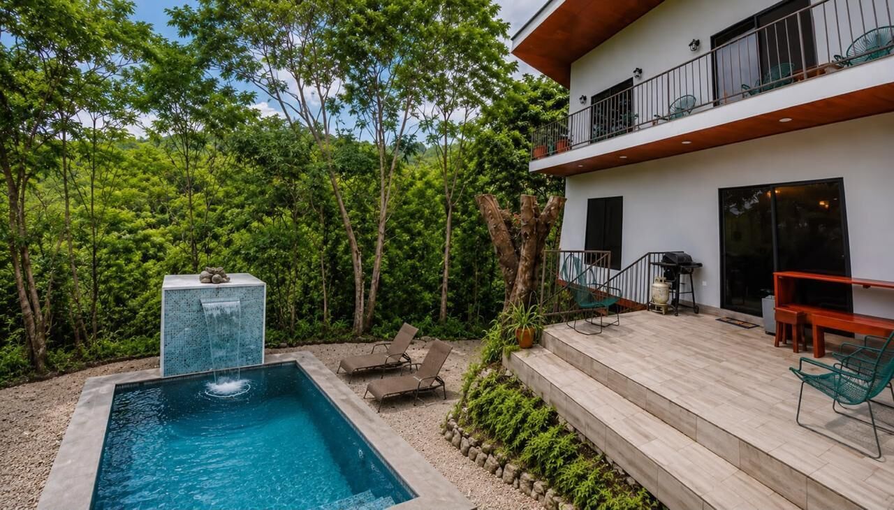 Une piscine agrémentée d’une cascade, un espace salon extérieur et un bâtiment à deux étages doté d’un balcon.