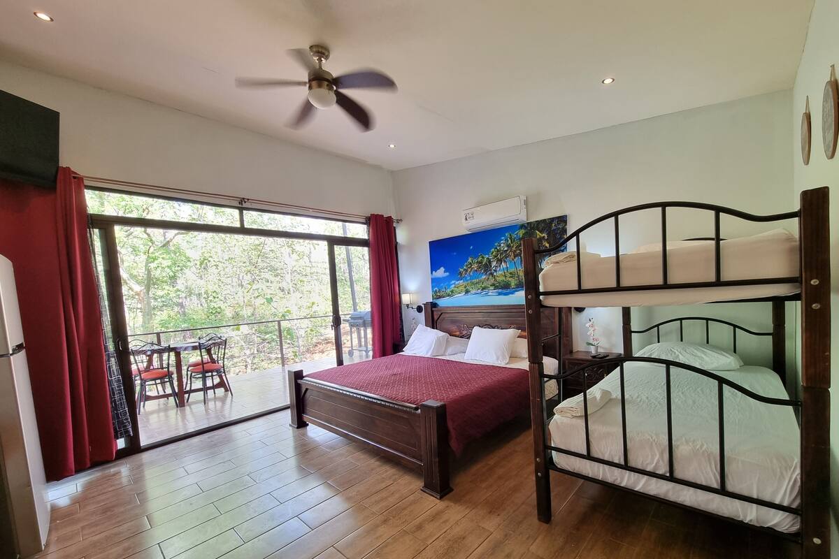 A bedroom with a bunk bed, a large window with curtains, a ceiling fan, and a painting on the wall.