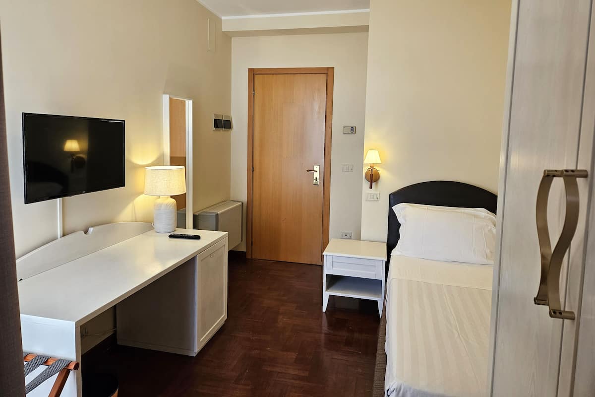 Een hotelkamer met een bed, een bureau met een televisie, een lamp en een deur.