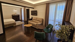 A hotel room with a bed, a sofa, a small table, two chairs, a TV, and a potted plant. - Giardino Dei Principi (Citta Sant'Angelo)