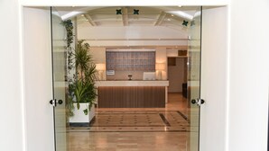 A reception area with a glass door, a reception desk, a large potted plant, and a patterned carpet. - Giardino Dei Principi (Citta Sant'Angelo)