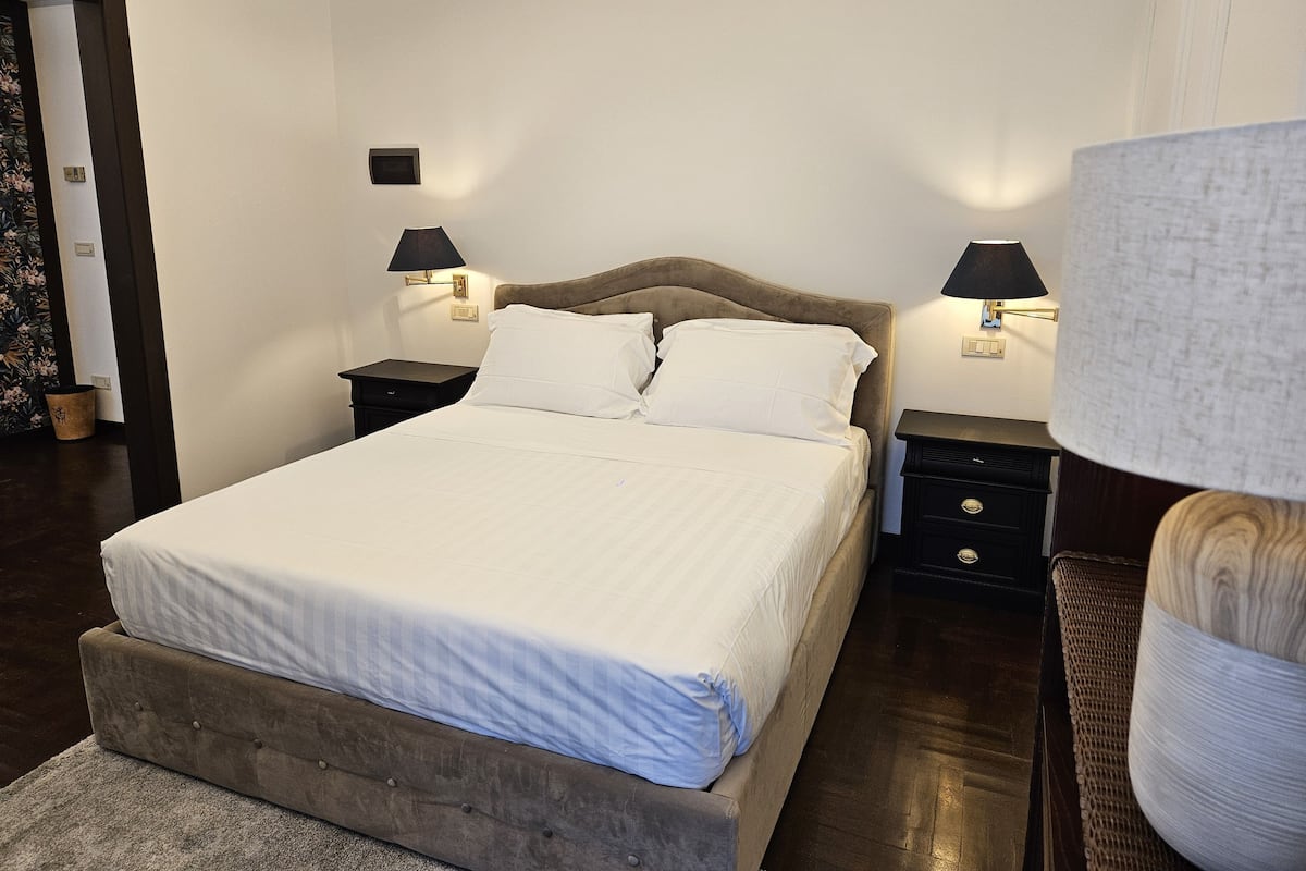 Een keurig opgemaakt slaapkamer met een groot bed, twee nachtkastjes en twee wandlampen.