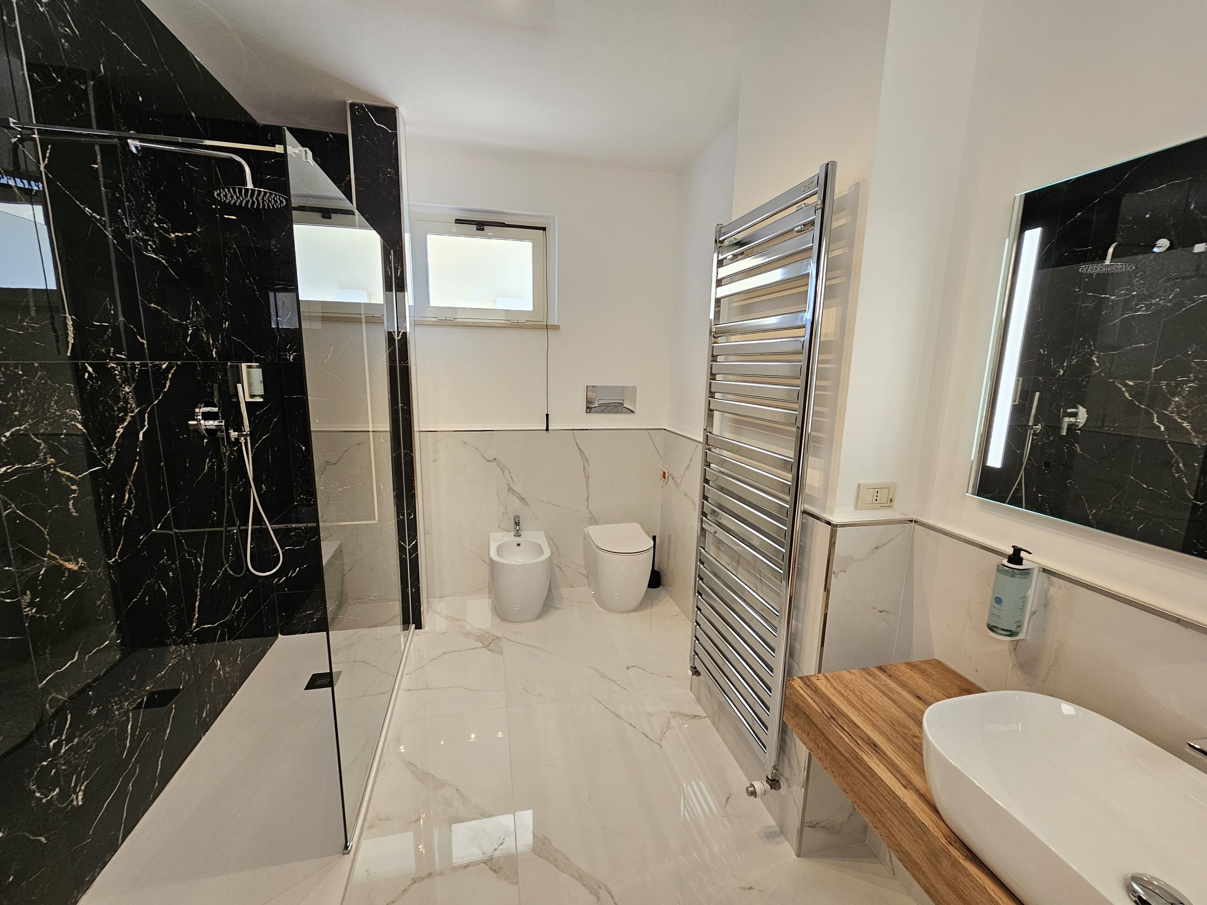 A modern bathroom with a glass-enclosed shower, a bidet, a toilet, a towel rack, and a wooden vanity with a sink.