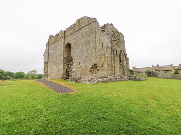 Un edificio histórico de piedra con techo derrumbado y puerta arqueada, rodeado por un campo cubierto de hierba.