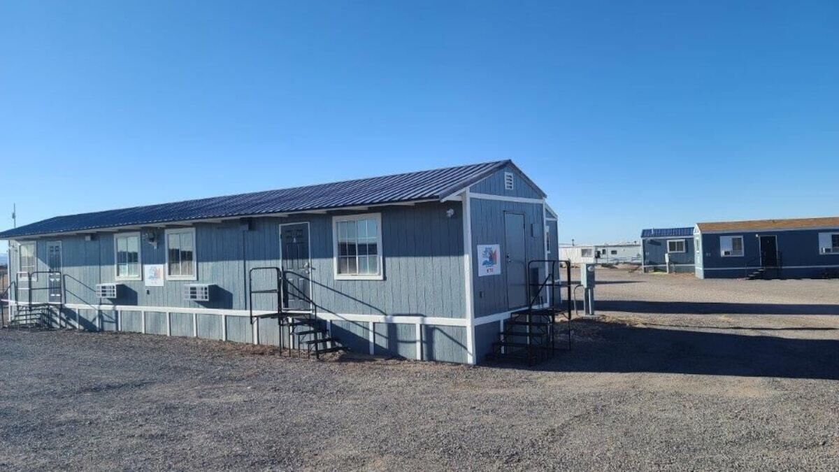 A single-story building with a metal roof, a front staircase, and a gravel ground.