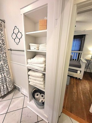 A room with a white wardrobe containing folded towels and a basket with toiletries. - The Crescent House (Hutchinson)