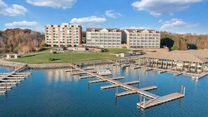 A marina with docked boats, a large building complex with multiple floors, and a grassy area in the foreground.