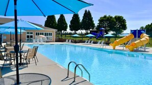 A swimming pool with lounge chairs and umbrellas, a slide, and a building in the background.