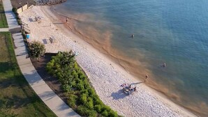 An aerial view of a beach with a paved walkway, clear water, and people swimming.
