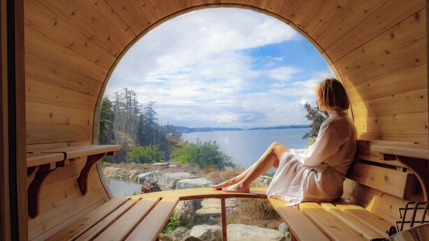 A wooden cabin with a circular window offering a view of a lake and forest. - Lightwater Cove (Salt Spring Island)