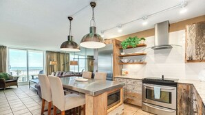 Een moderne keuken met een centraal eiland, roestvrijstalen apparatuur en een groot raam met uitzicht op een balkon.