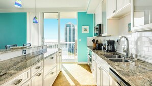 A modern kitchen with white cabinets, granite countertops, and a view of tall buildings through a glass door. - Seaside Family Oasis Hideaway (Galveston)