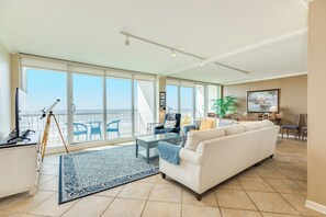 Een ruime woonkamer met een groot raam, een witte bank, een glazen salontafel en een statief.