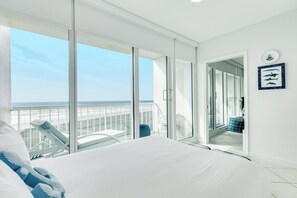 Ein Hotelzimmer mit einem großen Bett, einem Balkon mit Meerblick und einer Tür zu einem Badezimmer.