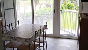 A dining area with a table and chairs, a refrigerator, and a view through a glass door to an outdoor area with a fence and greenery. - Guest House L'orto di Antonio, surrounded by greenery a few steps from the sea  (Palinuro)