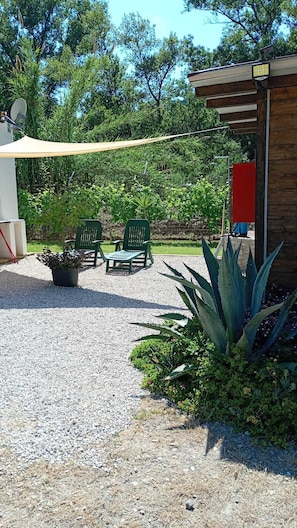Un espace patio avec un sol en gravier, deux chaises vertes, une table et un bâtiment en bois avec une porte rouge.